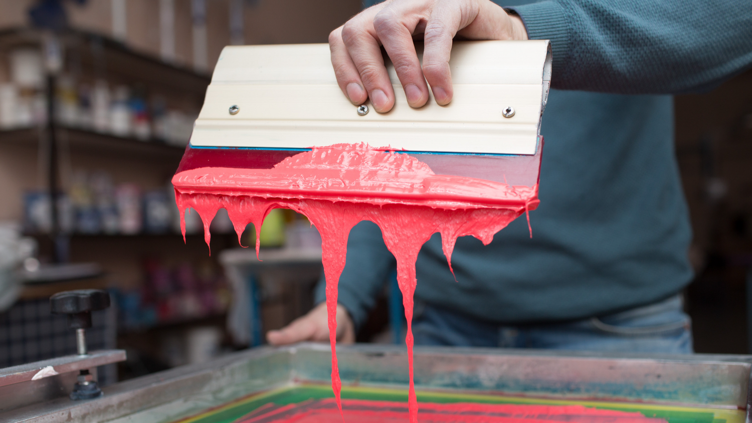 Screen printing process: using a squeegee to apply ink through a mesh screen onto a custom garment, showcasing the process of screen printing for custom apparel.